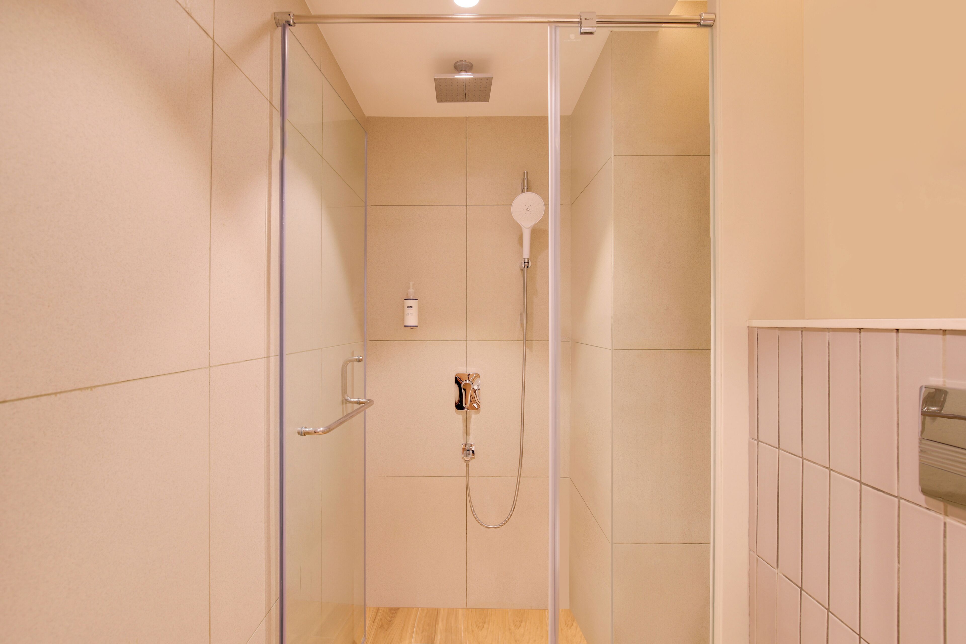 A glass-enclosed shower with a handheld showerhead and a wall-mounted faucet.