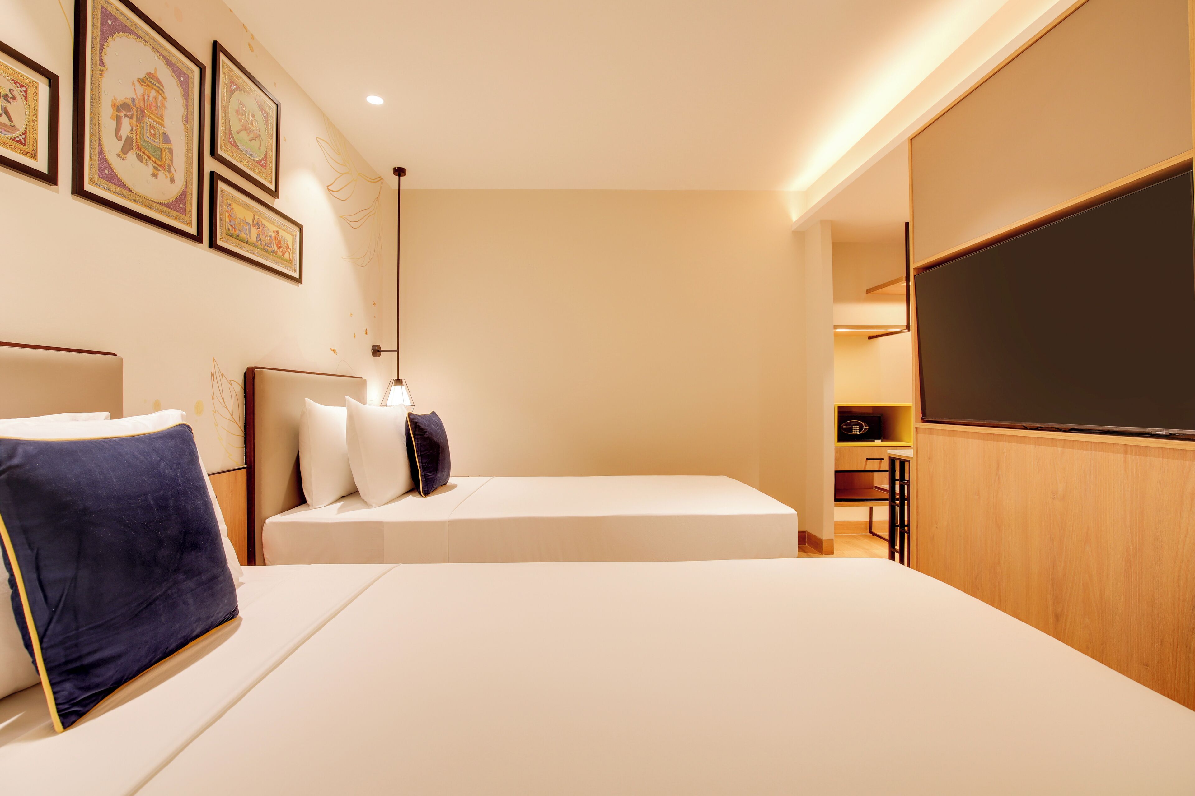 Ett hotellrum med en säng, kuddar, en platt-TV och inramade konstverk på väggen.