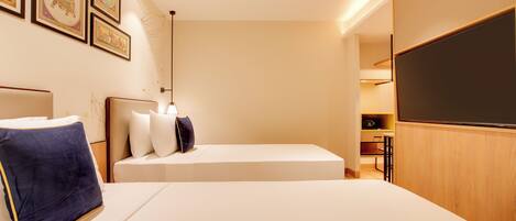 A hotel room with a bed, pillows, a flat-screen TV, and framed artwork on the wall.