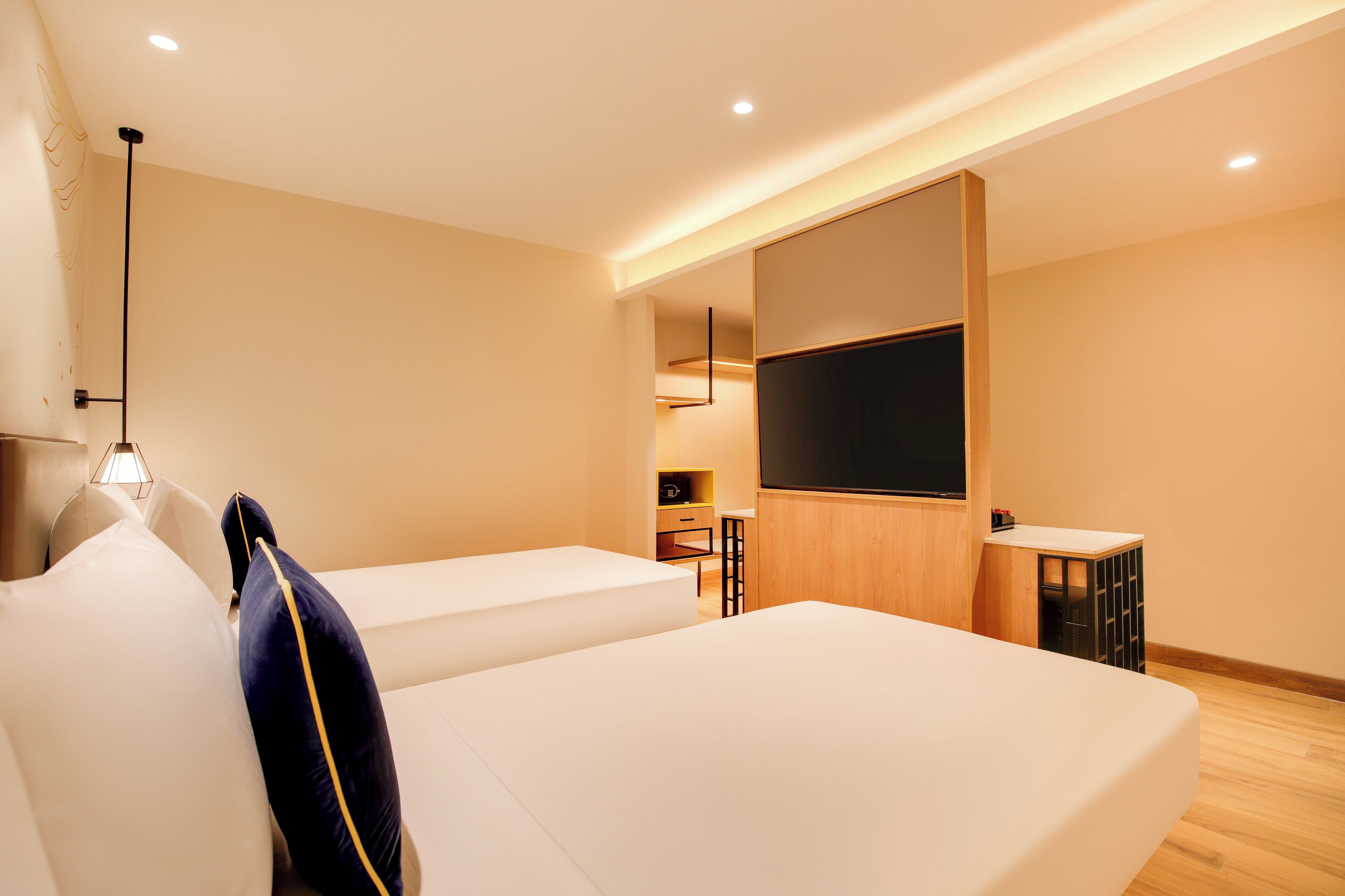 Una habitación de hotel moderna con dos camas, un televisor de pantalla plana, una kitchenette pequeña y piso de madera.