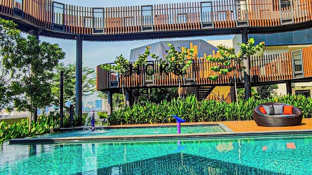 A modern outdoor pool area with a wooden deck, lounge chairs, and a view of the city skyline. - KL City View at Trion 2 by HCK (Kuala Lumpur)
