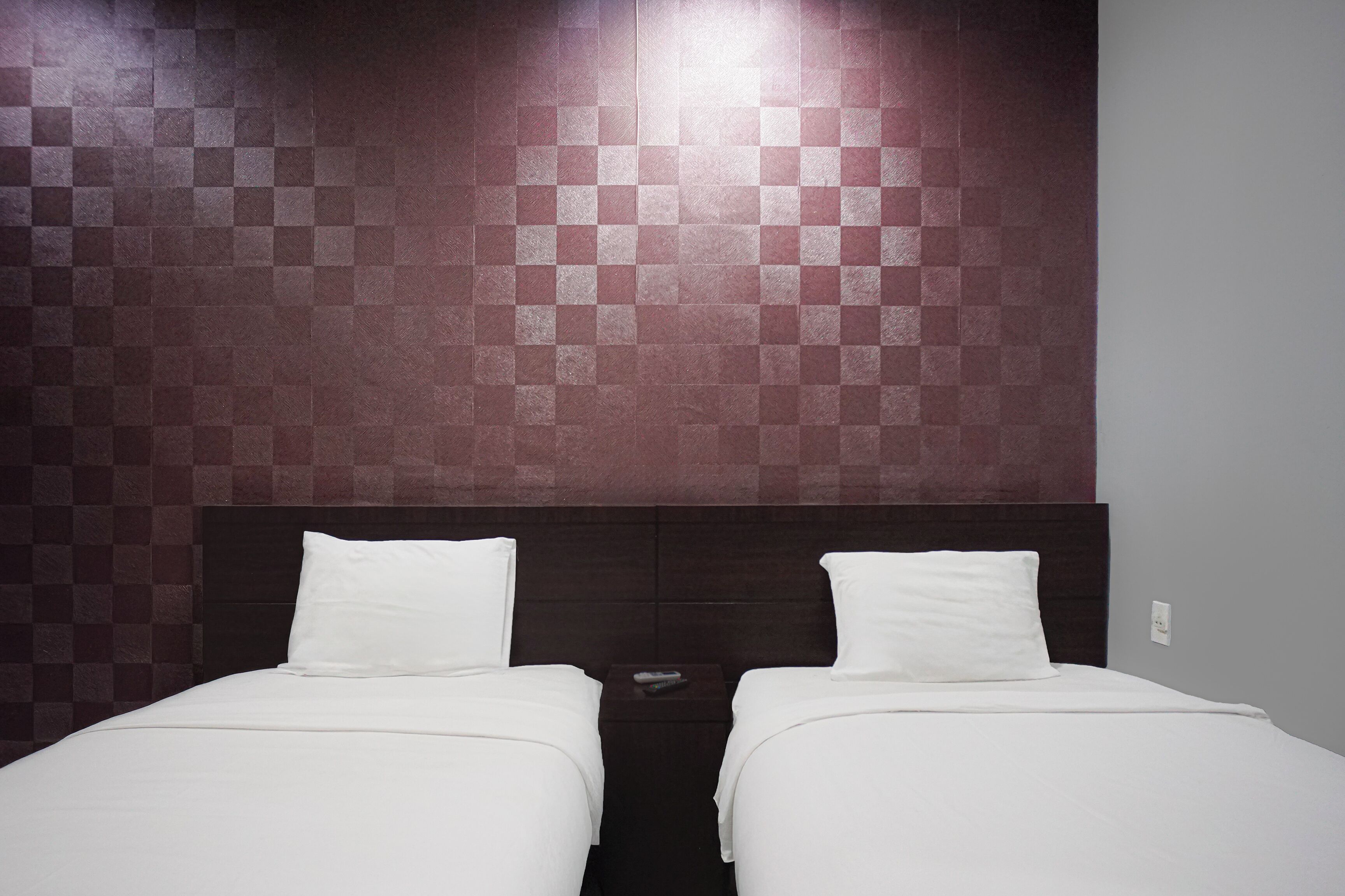 Une chambre d’hôtel avec deux lits simples, une tête de lit sombre et un motif à carreaux sur le mur.