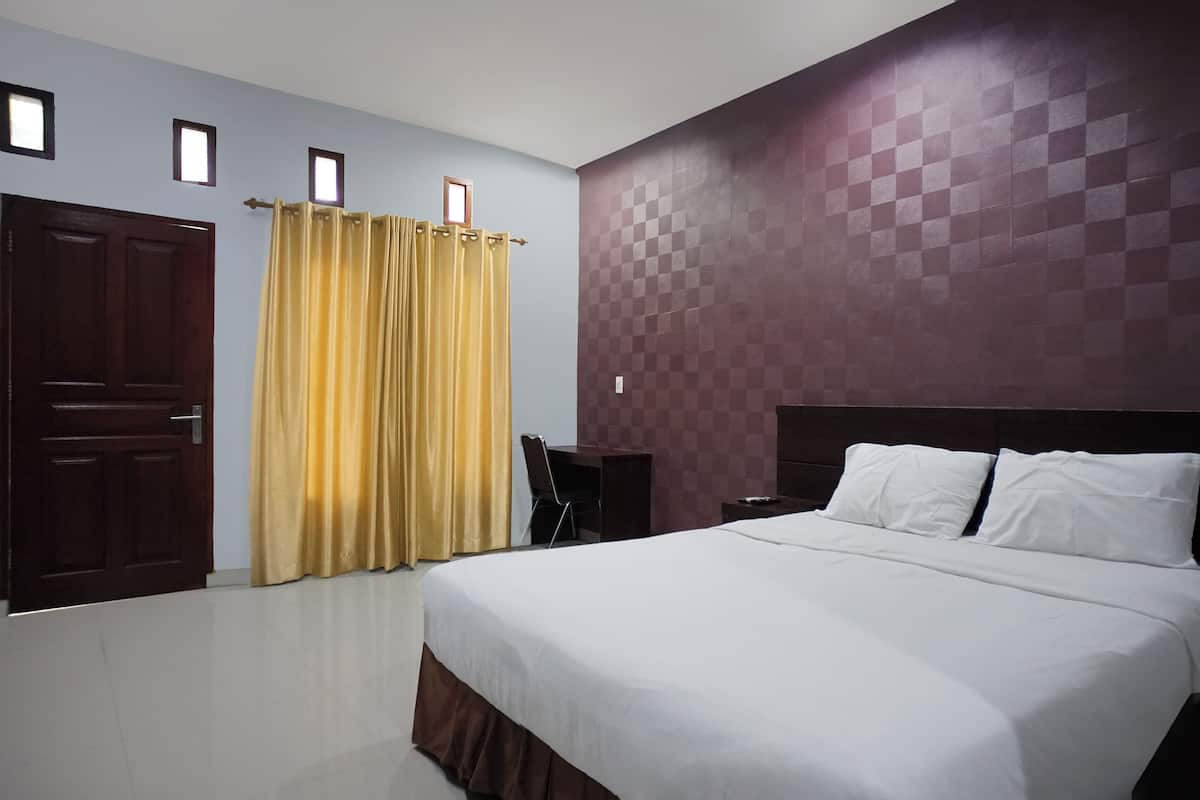 Ein Hotelzimmer mit einem großen Bett, einem Schreibtisch und einem Stuhl. An der Wand befinden sich drei kleine Fenster und eine Tür.