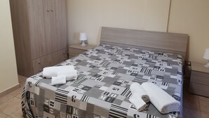 Un lit bien fait, recouvert d’une couvre-lit à motifs, une armoire en bois et une table de chevet avec une lampe.