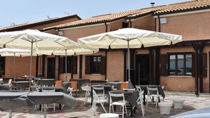 Un espace extérieur aménagé avec des tables et des chaises, protégé par des parasols, situé devant un bâtiment en briques doté de fenêtres et d’un toit en tuiles.