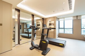 A modern gym with exercise equipment, large windows, and a view of the city.