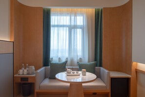 A cozy seating area with a round table, a sofa with teal cushions, and a window with sheer curtains. - Ji Hotel Guangzhou Baiyun Airport Terminal 2 (Guangzhou)