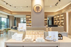 A modern hotel lobby with a reception desk, neatly arranged gift boxes, and a large circular logo on the wall. - Ji Hotel Guangzhou Baiyun Airport Terminal 2 (Guangzhou)