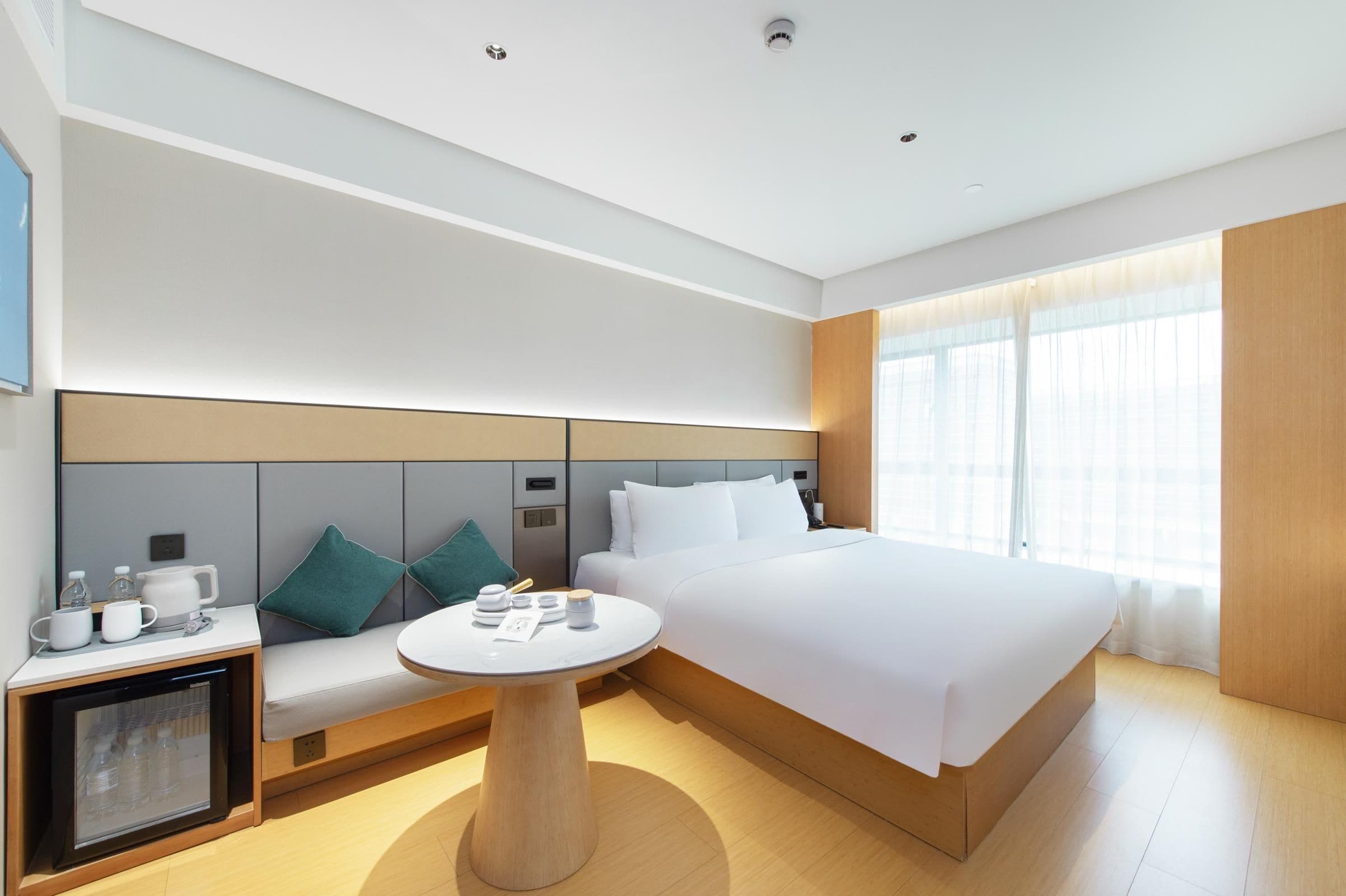 A modern hotel room with a large bed, a seating area with a table, and a minibar.