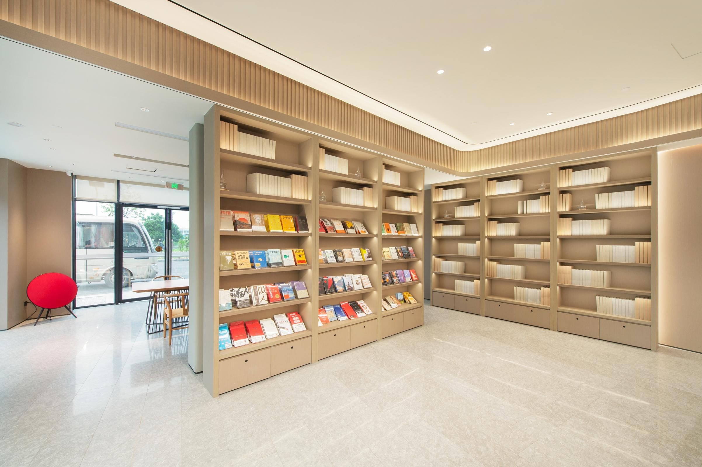 A modern library interior with bookshelves, a red chair, and a table.