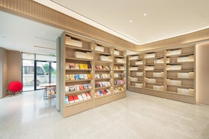 A modern library interior with bookshelves, a red chair, and a table. - Ji Hotel Guangzhou Baiyun Airport Terminal 2 (Guangzhou)