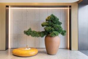 A modern lobby with a large potted tree, a wooden bench, and a tiled wall. - Ji Hotel Guangzhou Baiyun Airport Terminal 2 (Guangzhou)