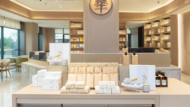 A modern hotel lobby with a reception desk, neatly arranged gift boxes, and a large circular logo on the wall. - Ji Hotel Guangzhou Baiyun Airport Terminal 2 (Guangzhou)