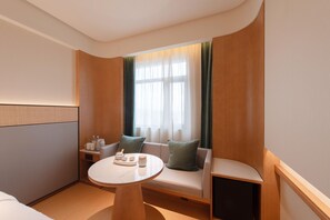 A modern hotel room with a sofa, a small table with a tray of items, a bedside table with a lamp, and a window with curtains. - Ji Hotel Guangzhou Baiyun Airport Terminal 2 (Guangzhou)