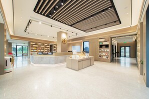 A modern hotel lobby with a central reception desk, a digital display, and a seating area. - Ji Hotel Guangzhou Baiyun Airport Terminal 2 (Guangzhou)