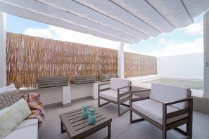 Un balcón con mobiliario blanco, una mesa de madera y vista al mar.