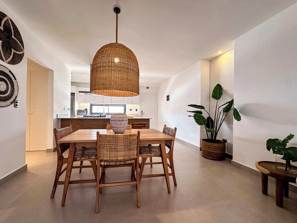 Un comedor con mesa y sillas de madera, una lámpara colgante tejida y una planta grande en maceta.