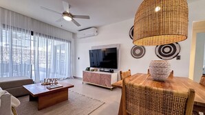 A modern living room with a wooden dining table, a sofa, a coffee table, a TV, and a ceiling fan.