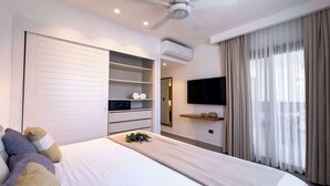 A modern hotel room with a large bed, built-in wardrobe, air conditioning unit, flat-screen TV, and a large window with curtains.