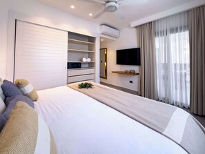 Une chambre d’hôtel moderne dotée d’un grand lit, d’une armoire intégrée, d’un système de climatisation, d’un téléviseur à écran plat et d’une grande fenêtre avec des rideaux.