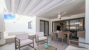 Un espacio exterior moderno con piscina, mobiliario blanco y una mesa de comedor con sillas.