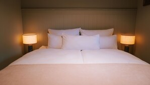 A neatly made bed with white linens and pillows, flanked by two bedside lamps.