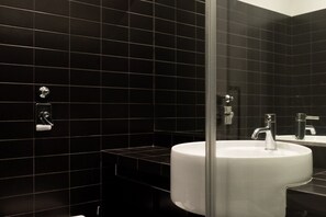 A modern bathroom with black tiled walls, a white sink, and a glass shower enclosure. - Modern and Spacious Studio in Duomo - Mirable PM (Milano)