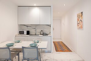 A modern kitchen with white cabinets, a marble backsplash, and a dining area with a white table and blue chairs. - Modern and Spacious Studio in Duomo - Mirable PM (Milano)