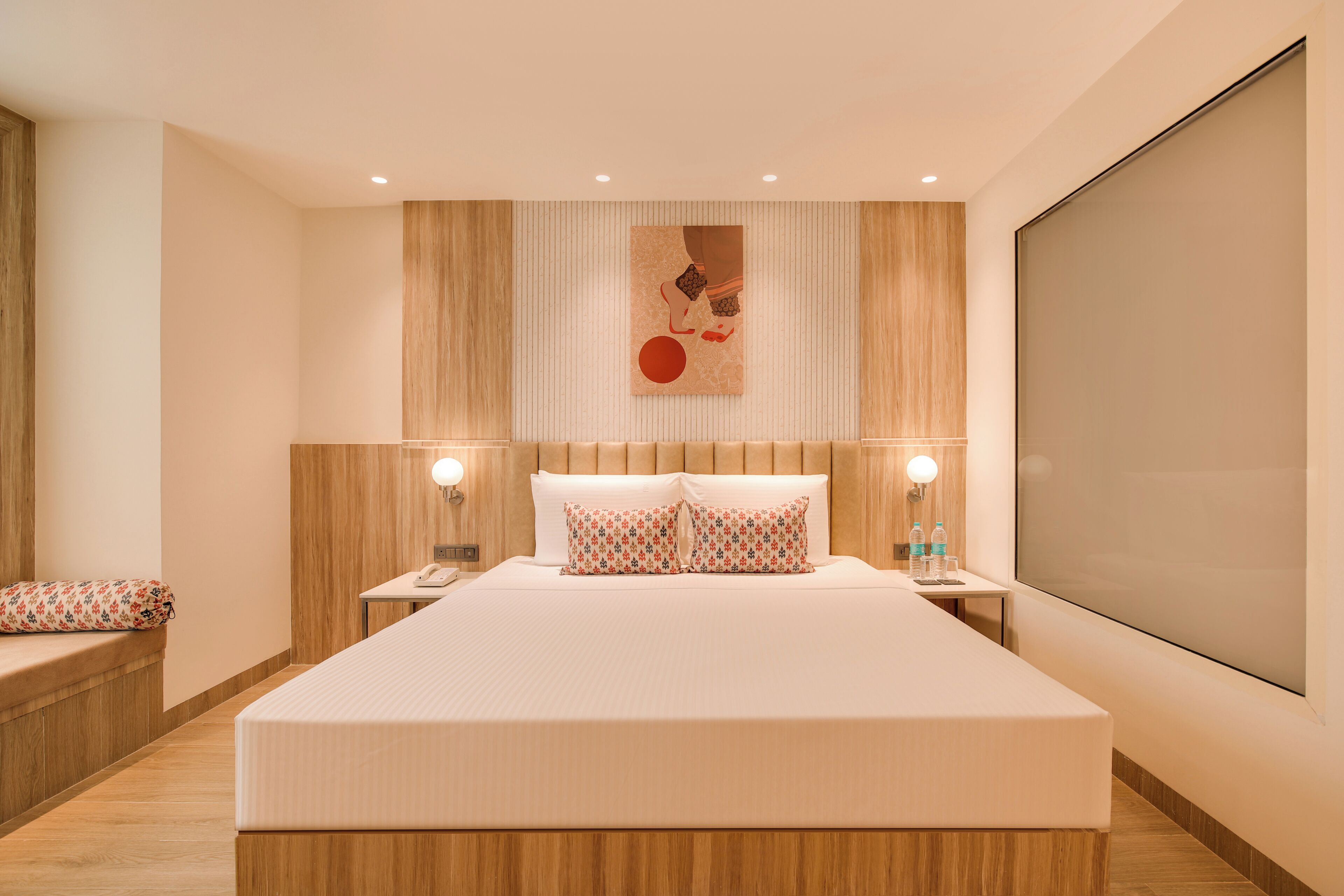 A modern hotel room with a large bed, wooden paneling, a large window, and a painting on the wall.