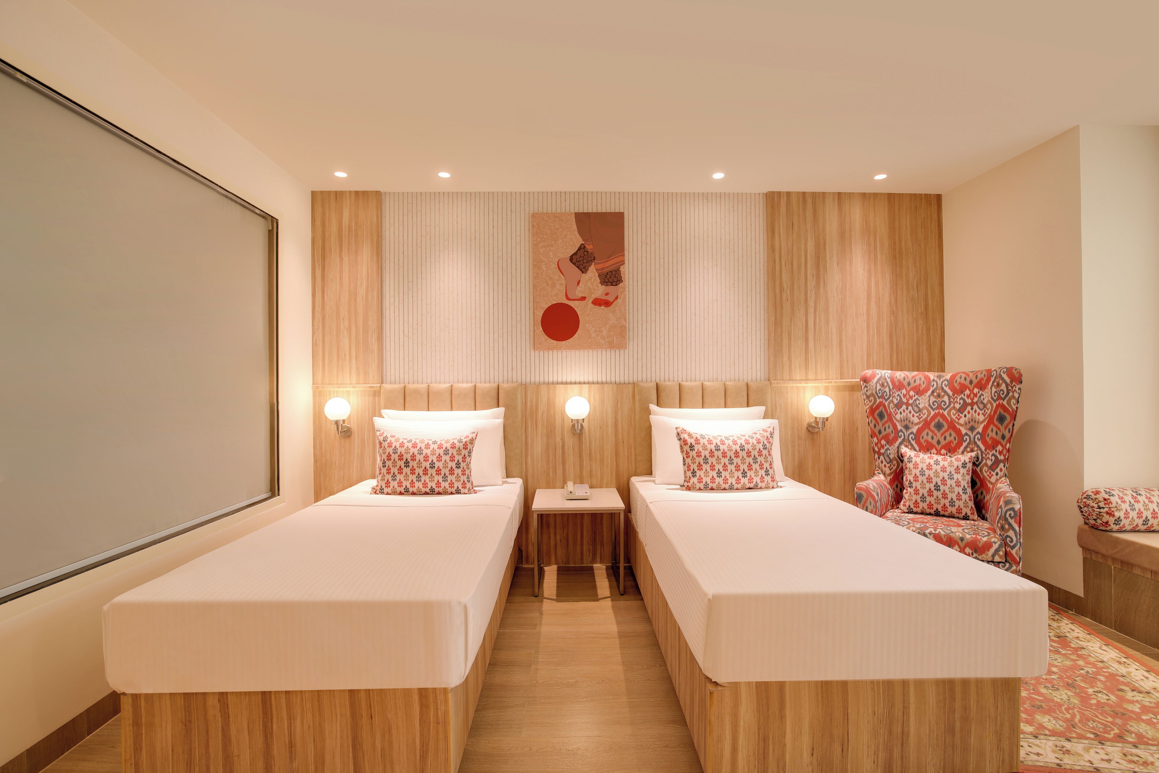 A hotel room with two beds, a small table, a chair, and a large window.