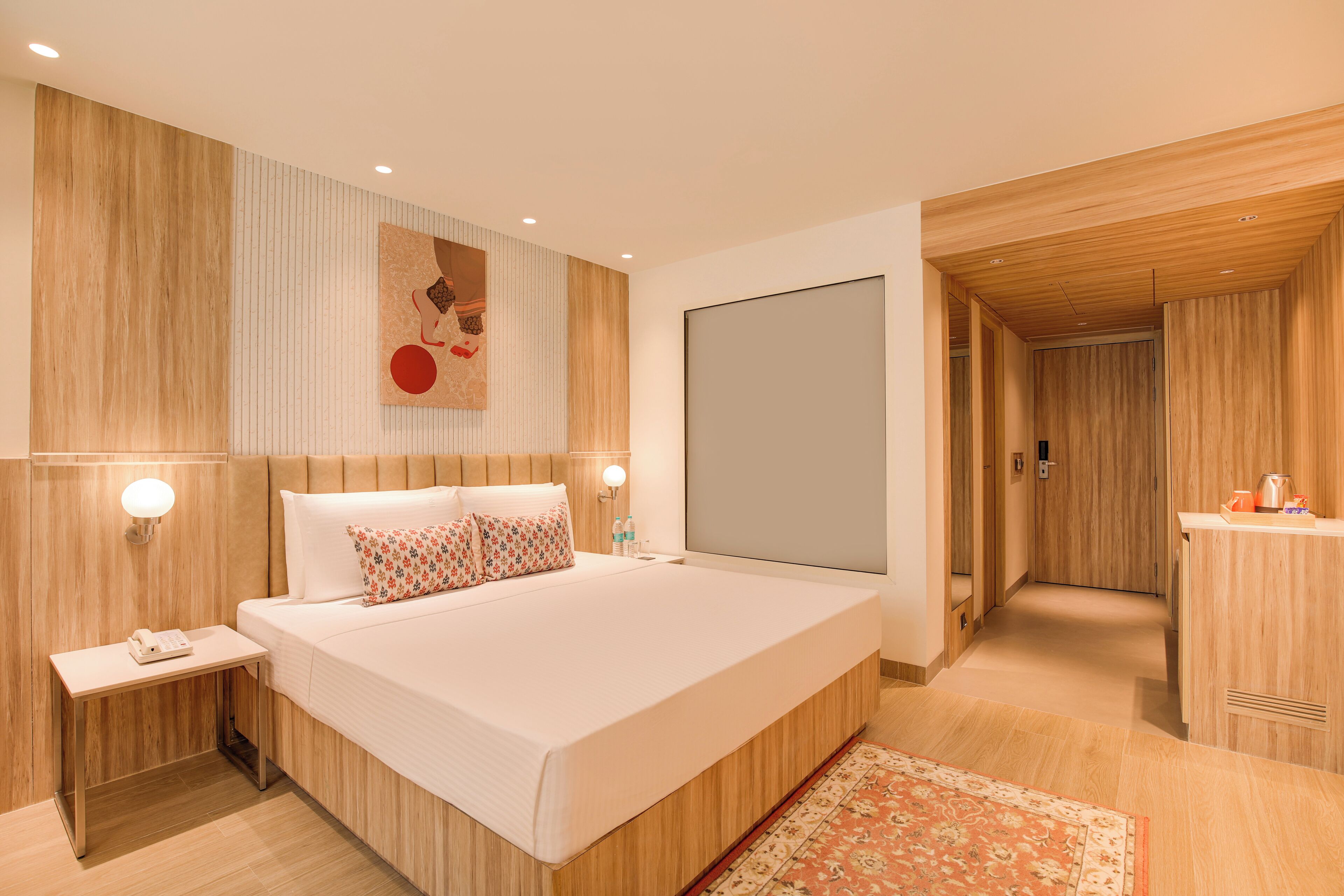 Une chambre d’hôtel moderne avec un grand lit, des panneaux de bois au mur, un téléviseur à écran plat, une table de chevet avec une lampe et un petit bureau avec un téléphone.