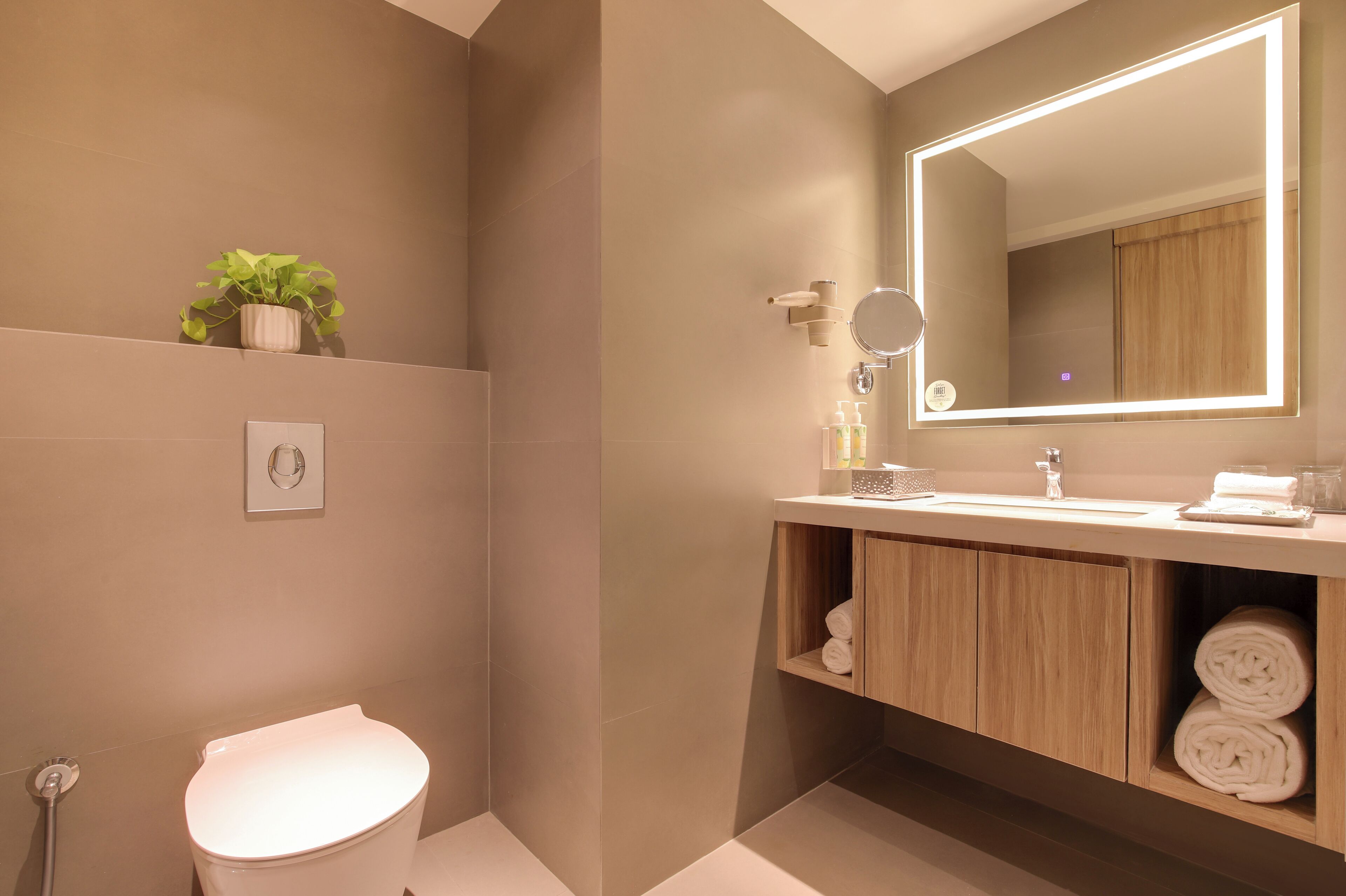 A modern bathroom with a large mirror, a toilet, and a sink area with towels and toiletries.