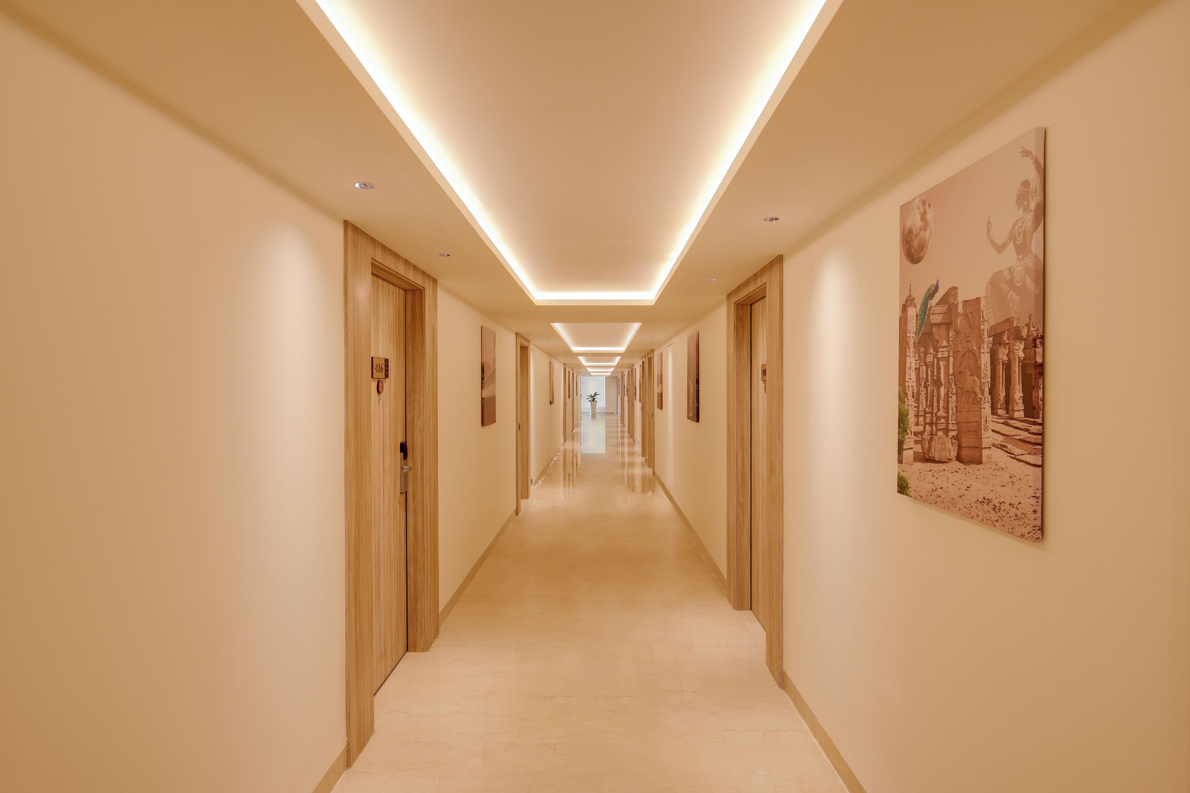 Un largo y estrecho pasillo con puertas de madera a ambos lados, alfombra de color claro e iluminación empotrada en el techo.