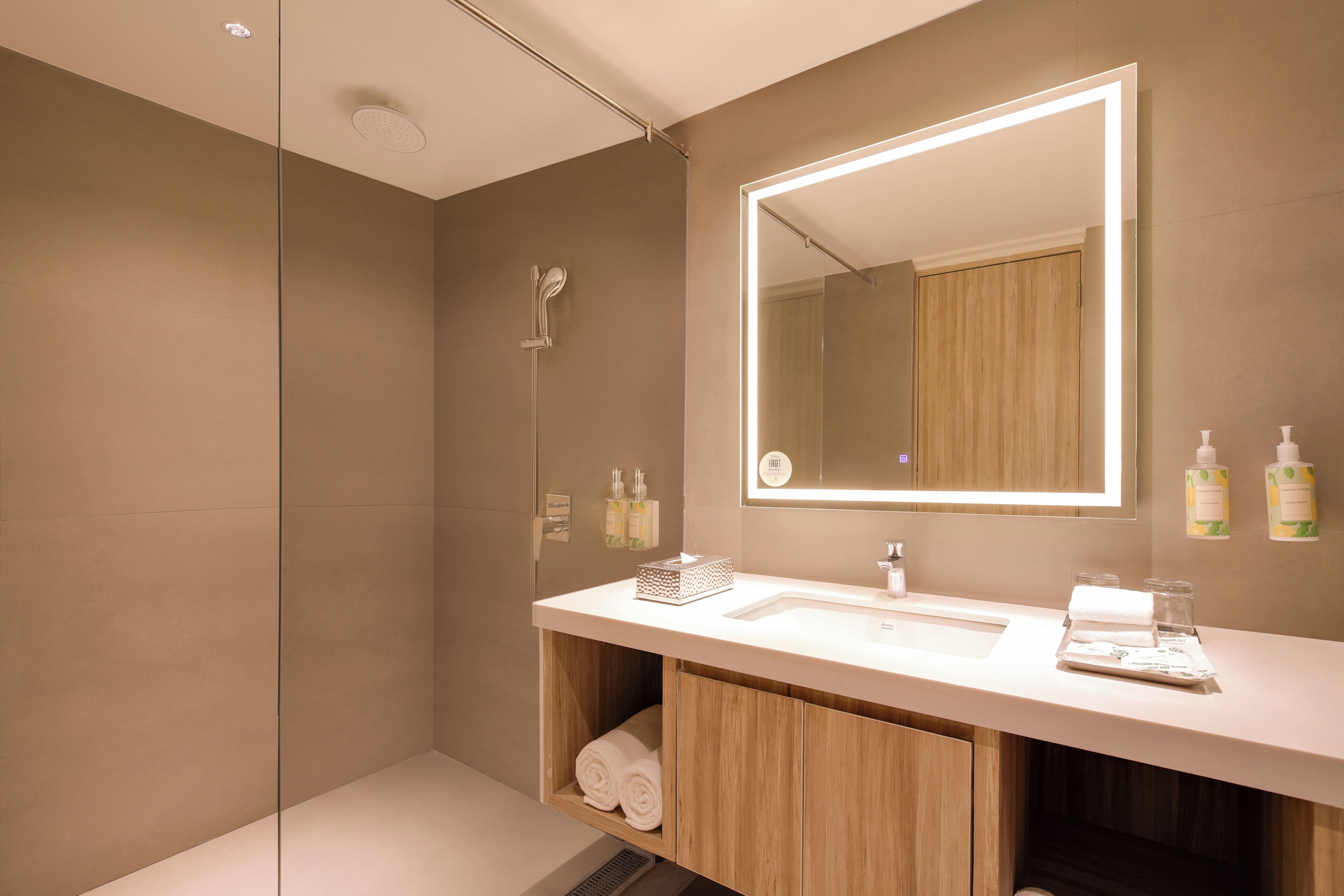 A modern bathroom with a large mirror, a shower, and a vanity with toiletries.