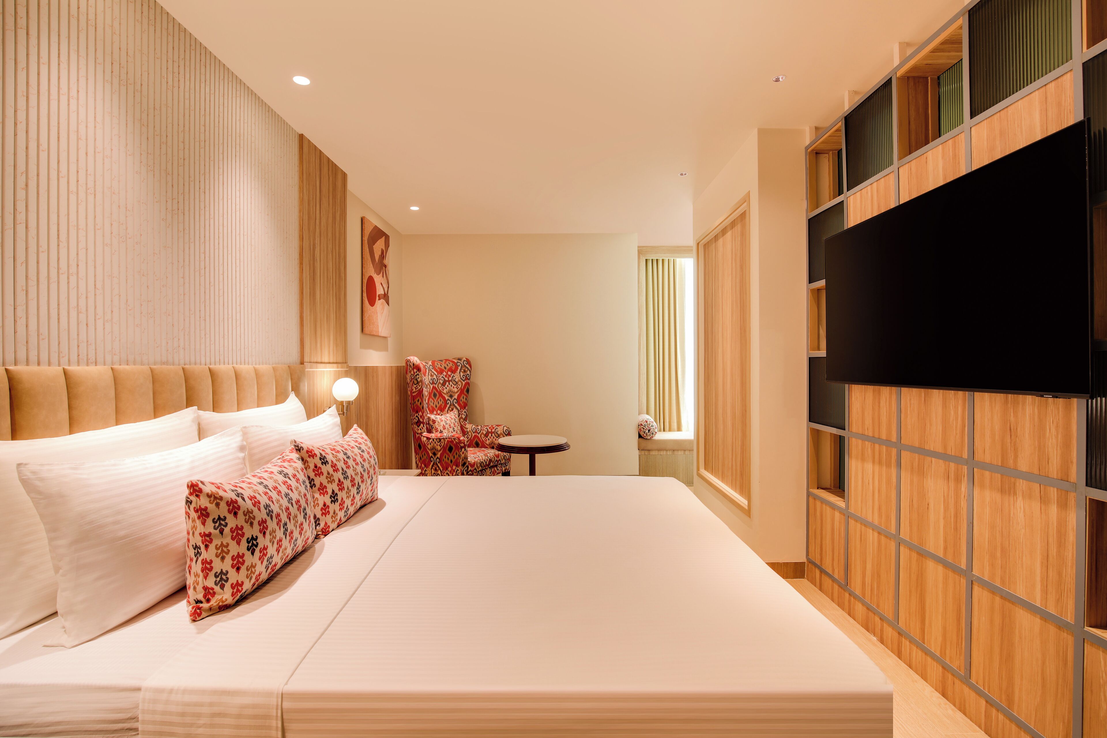 Una habitación de hotel moderna con una cama grande, un televisor, una mesita pequeña y una silla.