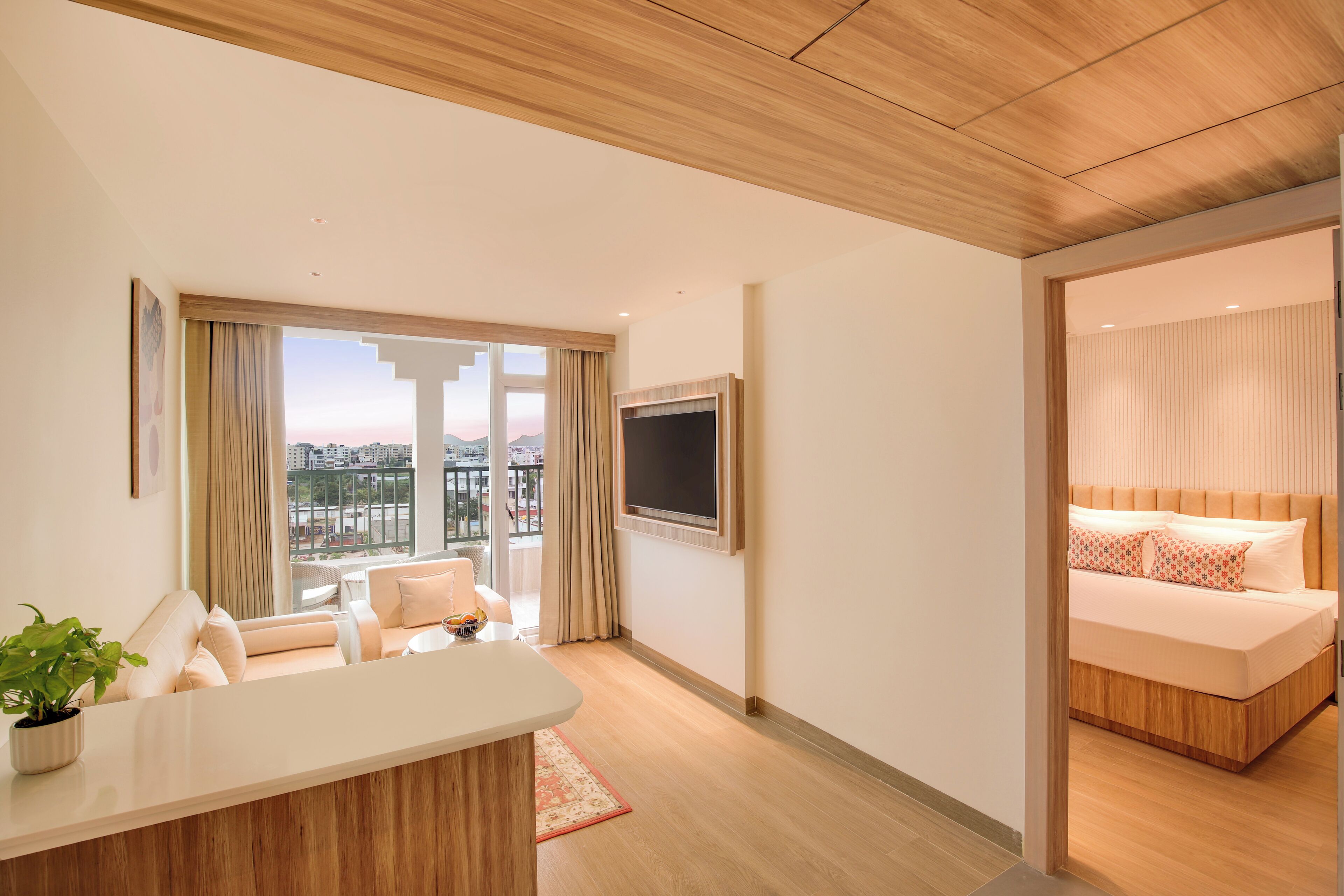 Una habitación de hotel moderna con un ventanal grande, un televisor de pantalla plana, un sofá y una cama con cabecero de madera.