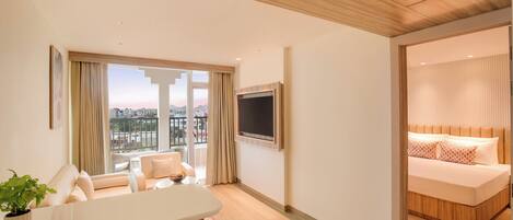 Una habitación de hotel moderna con un ventanal grande, un televisor de pantalla plana, un sofá y una cama con cabecero de madera.