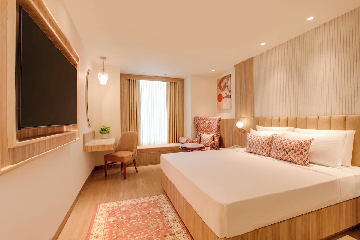 A hotel room with a large bed, a desk, a chair, a TV, and a window with curtains.