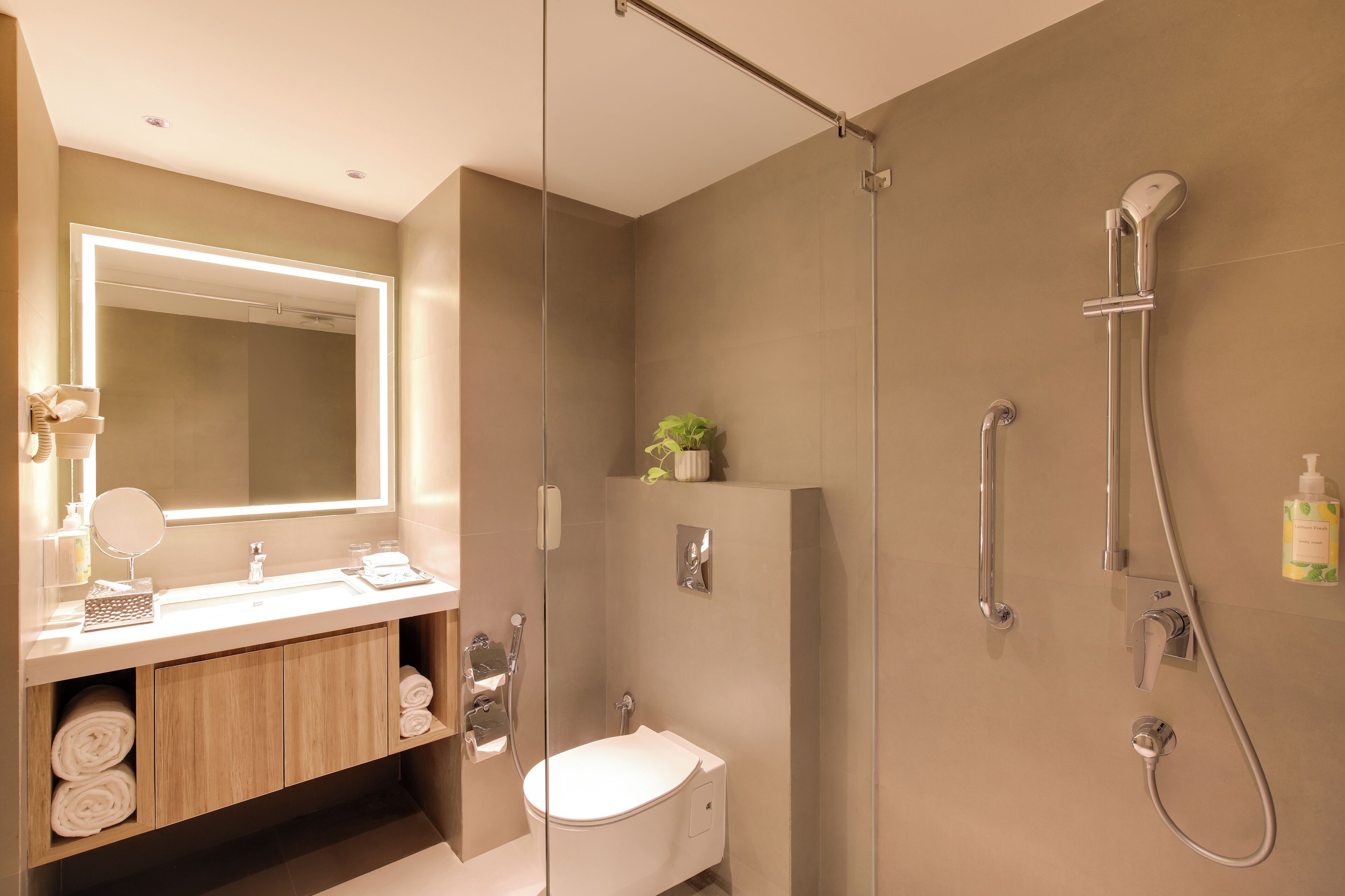 A modern bathroom with a glass-enclosed shower, a white sink with a mirror, and a wooden vanity with towels.