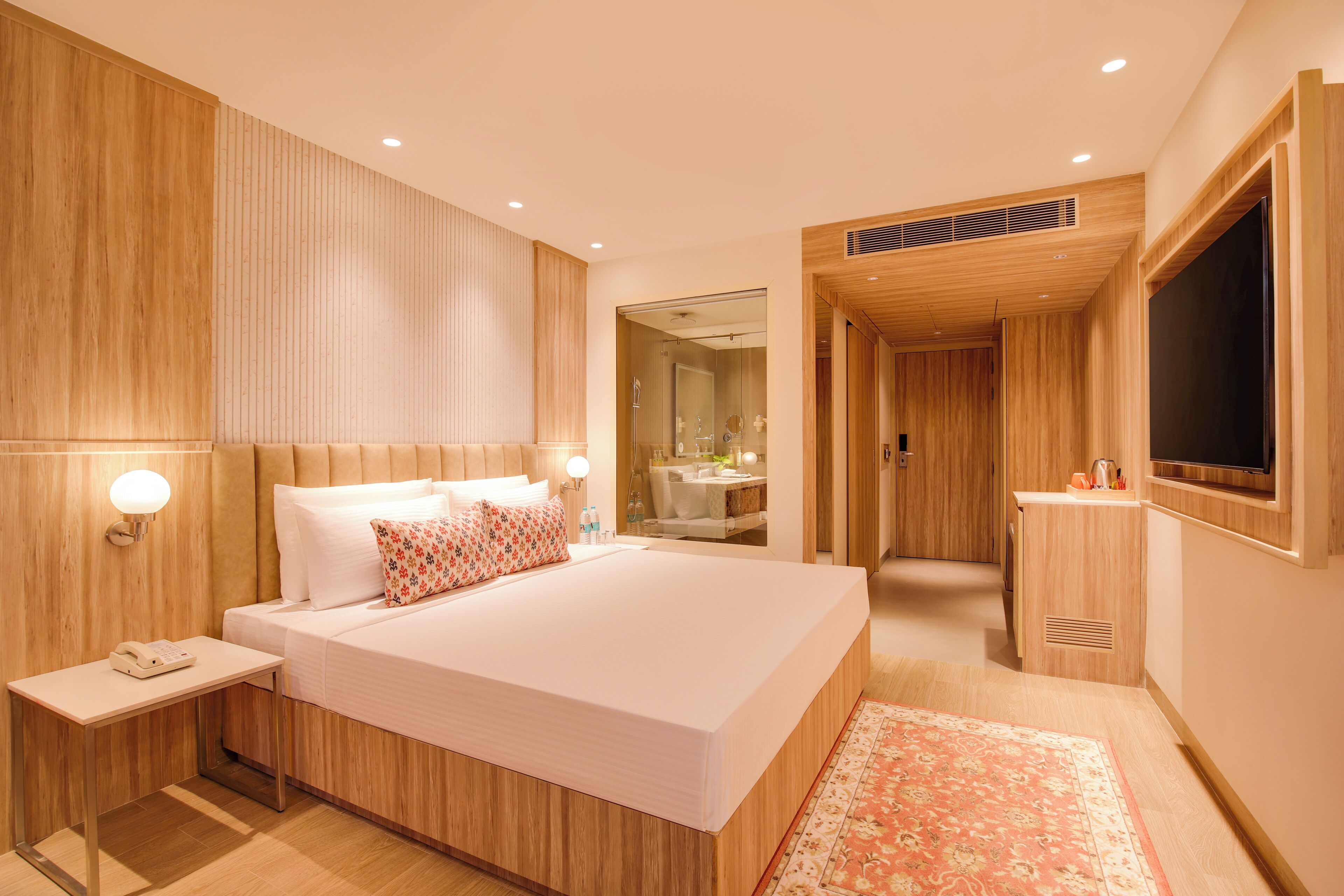 Una habitación de hotel moderna con una cama grande, mesitas de noche, un televisor y un baño visible a través de una puerta abierta.