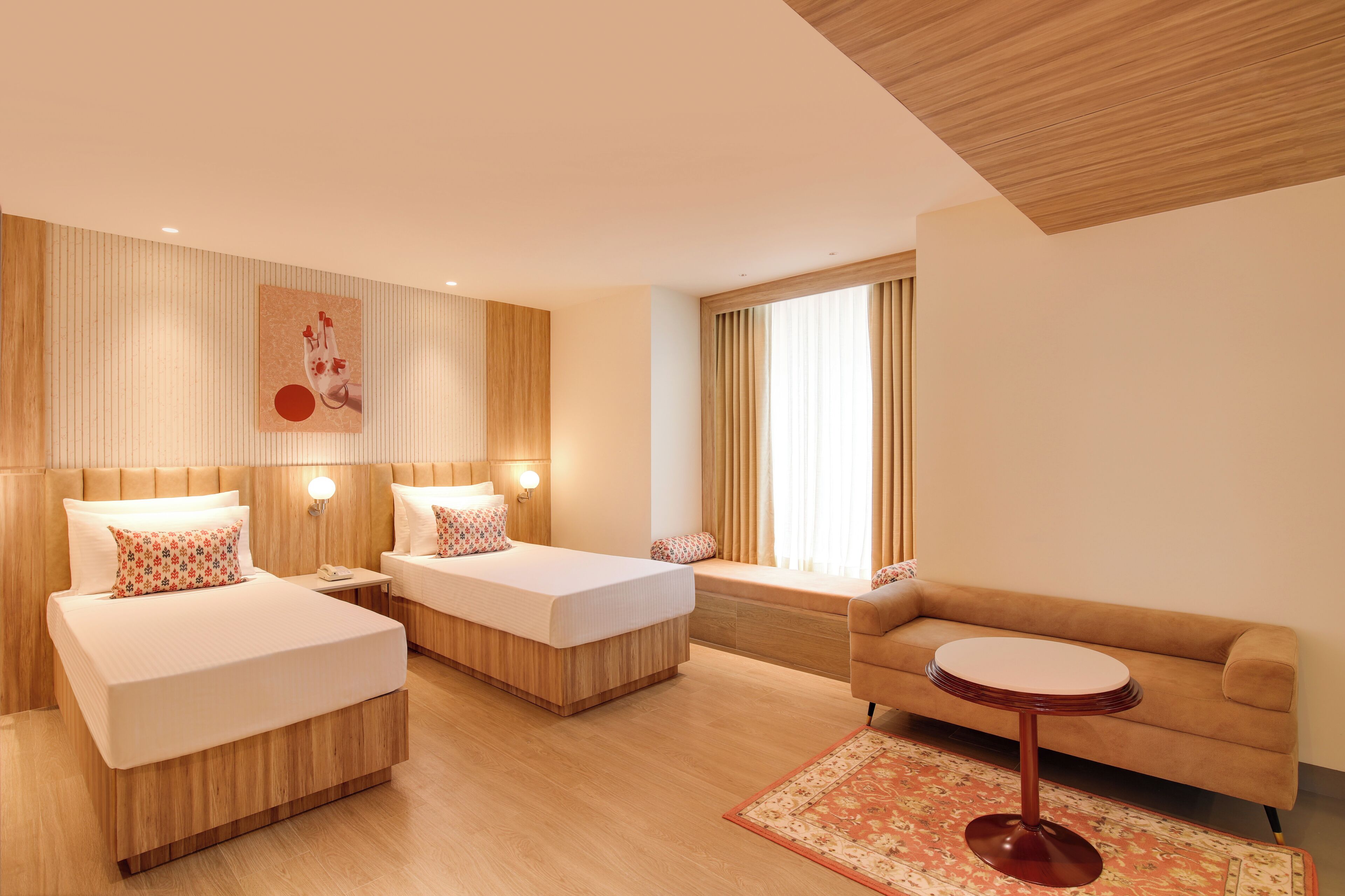 Una habitación de hotel moderna con dos camas, un sofá, una mesita redonda y un ventanal con cortinas.