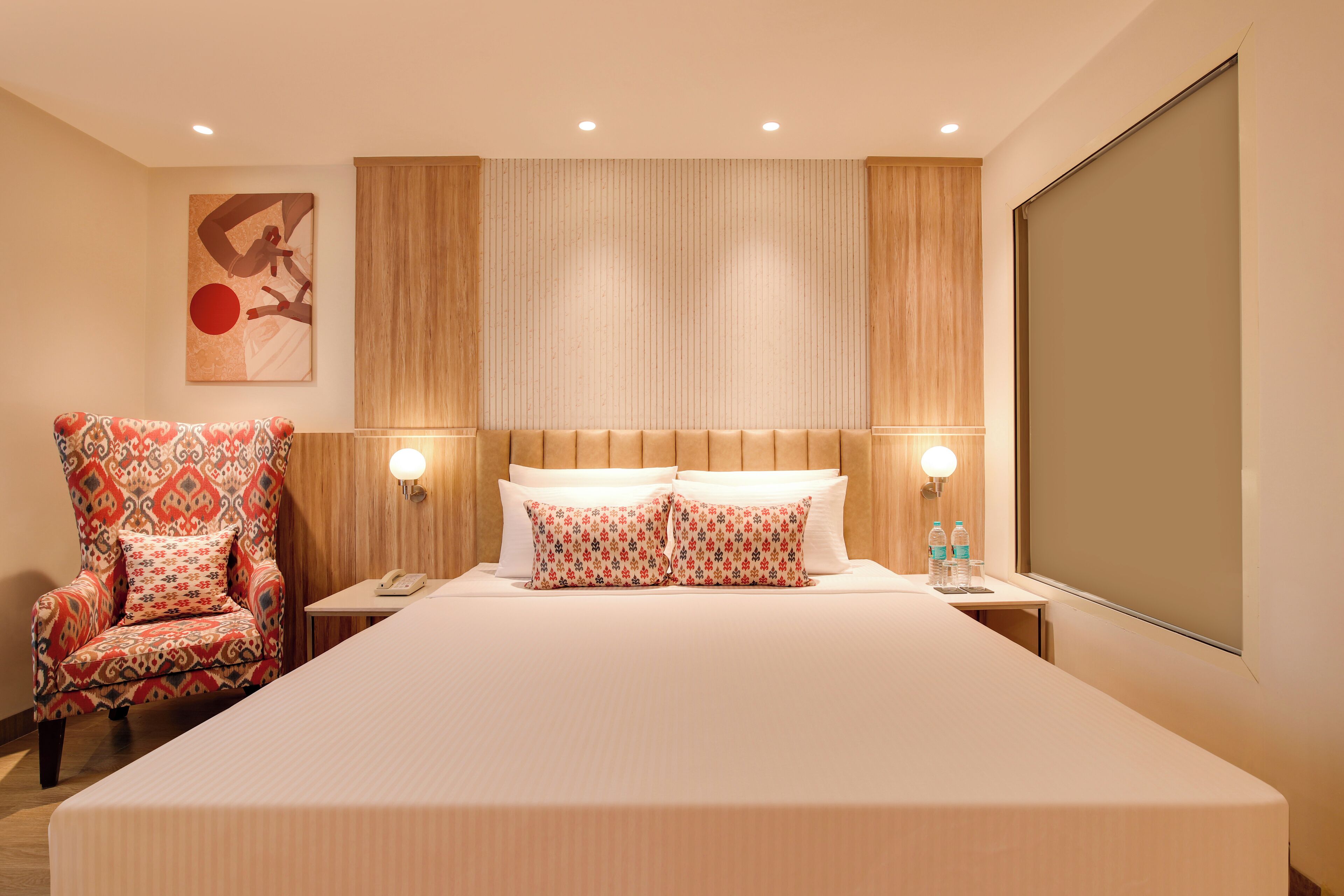 A hotel room with a large bed, two bedside tables, a chair, and a wall-mounted artwork.