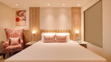 Een hotelkamer met een groot bed, twee nachtkastjes, een stoel en een kunstwerk aan de muur.