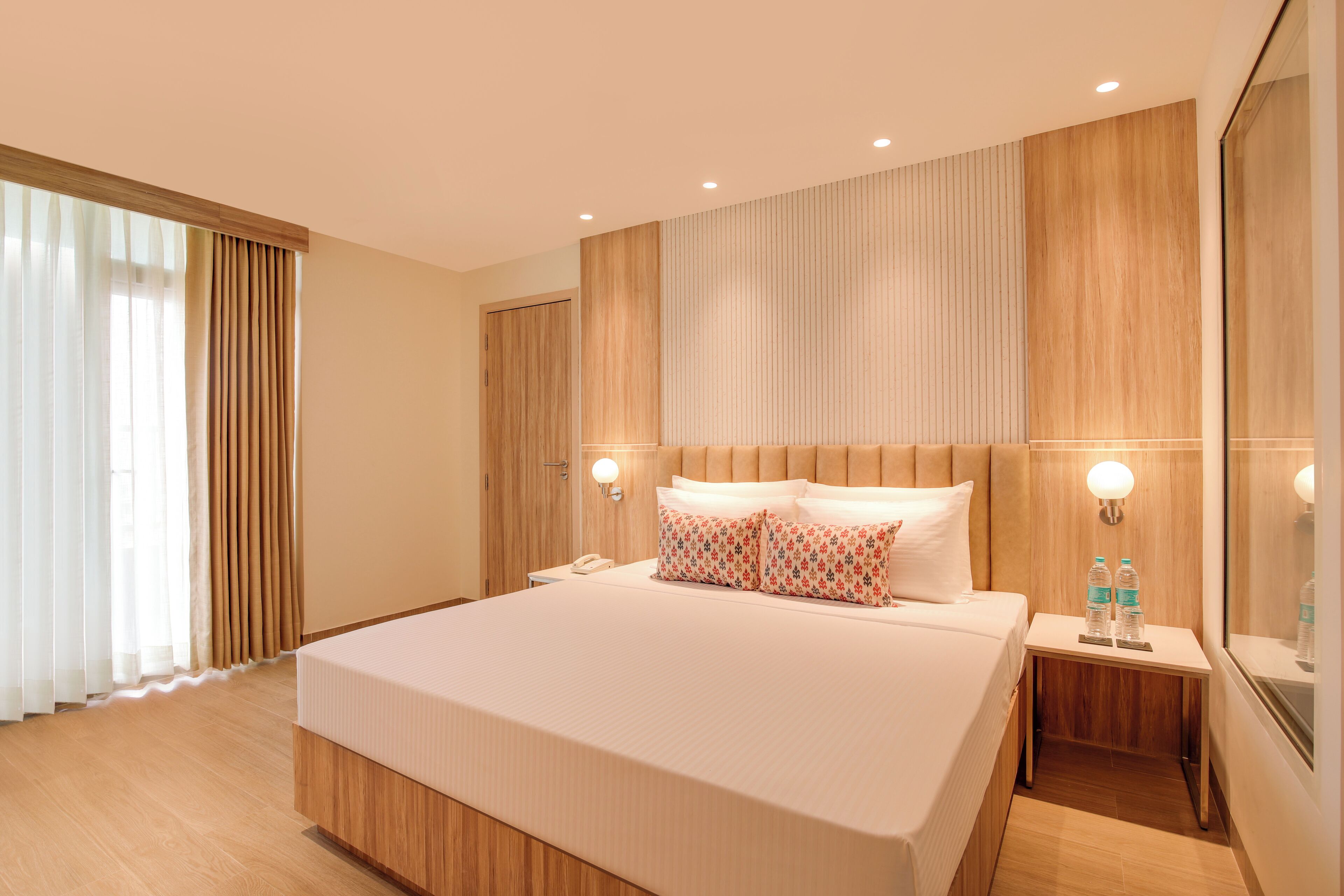 Una habitación de hotel moderna con una cama grande, paneles de madera, una mesita de noche con lámpara y un espejo.