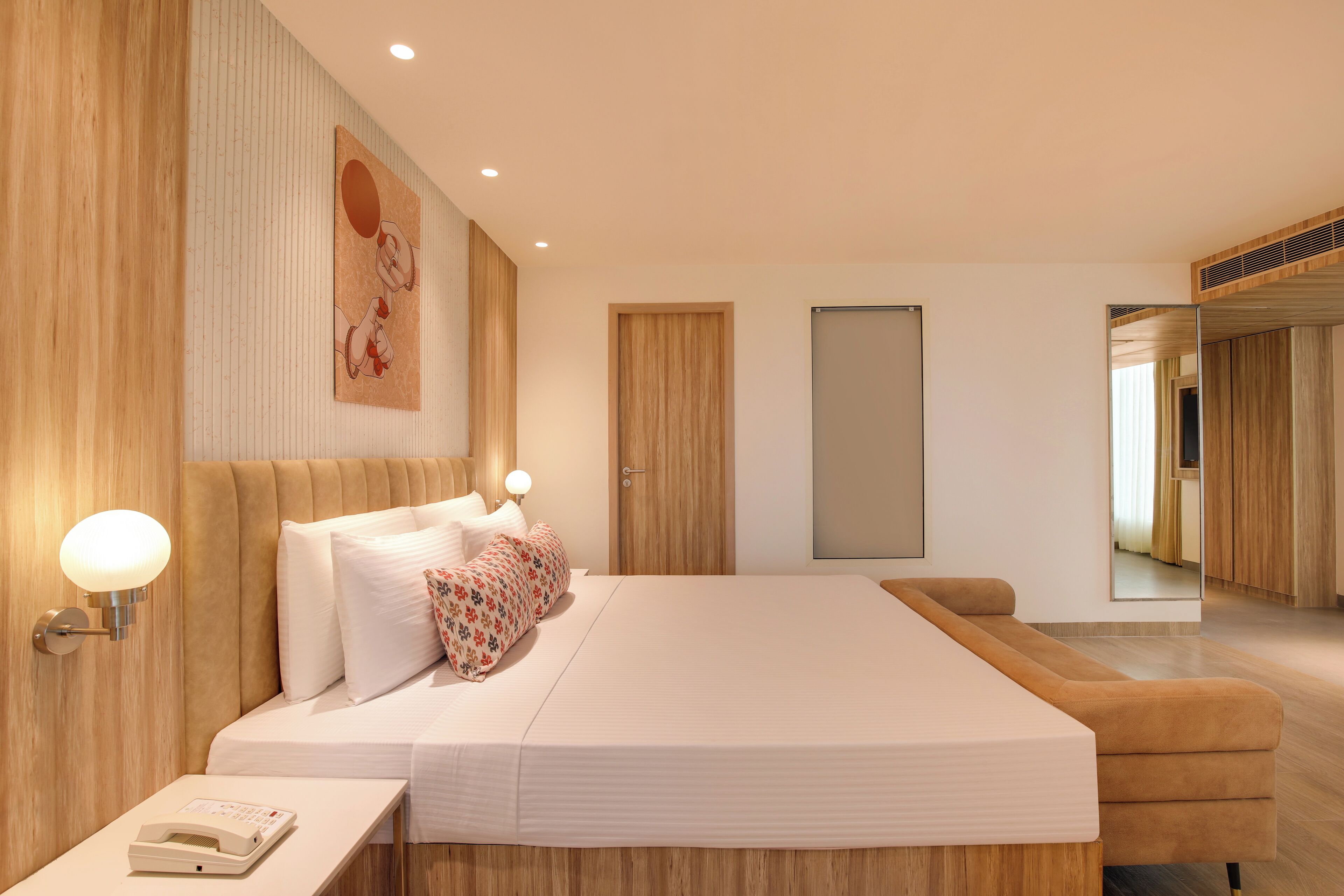 A modern bedroom with a large bed, bedside lamps, a wooden headboard, a bedside telephone, and a mirror on the wall.