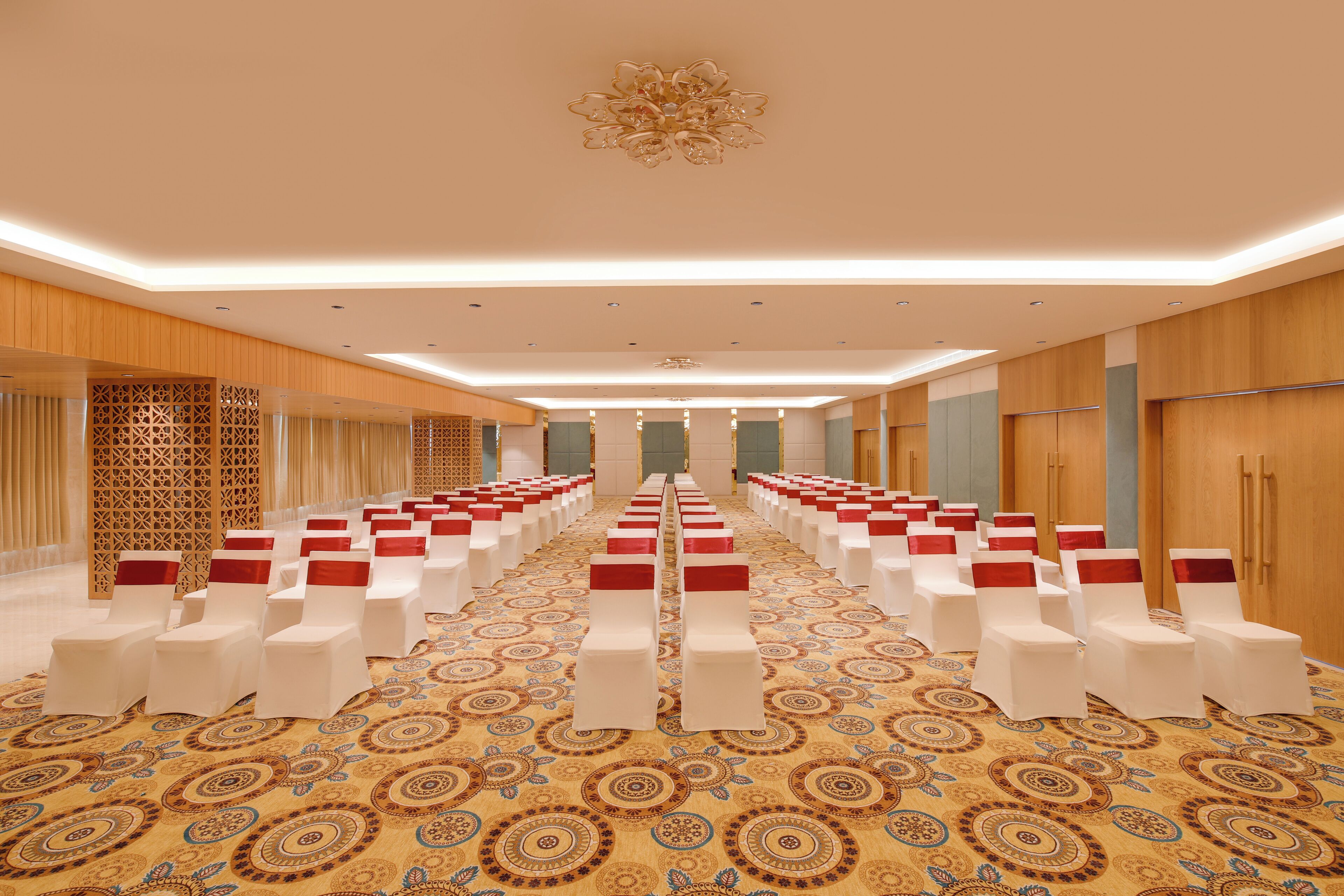 A conference room with rows of white chairs and red sashes, a patterned carpet, and wooden paneling on the walls.