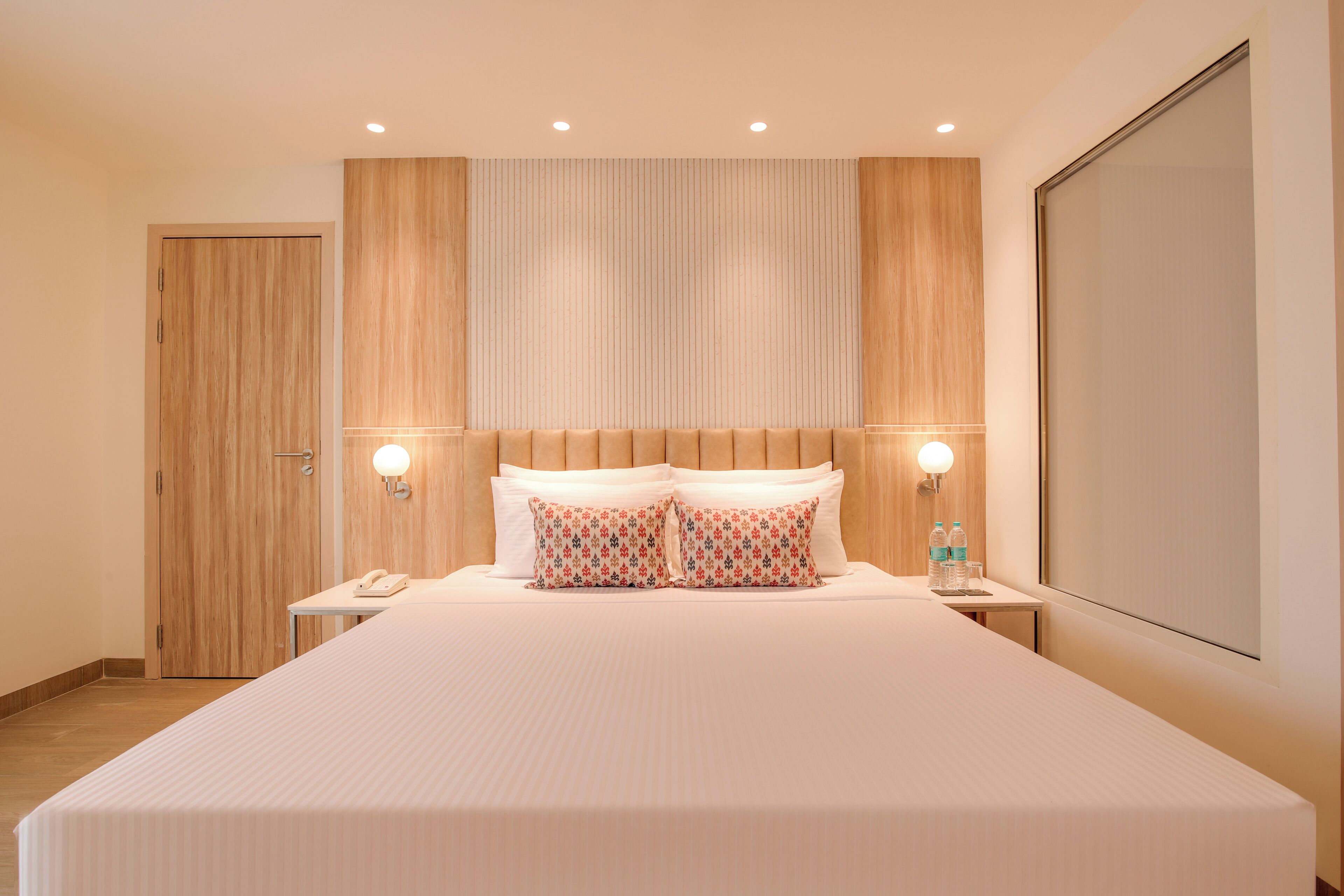 A hotel room with a large bed, two bedside tables, a wooden wardrobe, and a large window.
