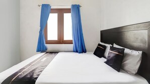 A single bed with a white mattress, a dark headboard, and two pillows. Blue curtains are tied at the top of the window. - OYO 94780 Blessing Homestay (Surabaya)