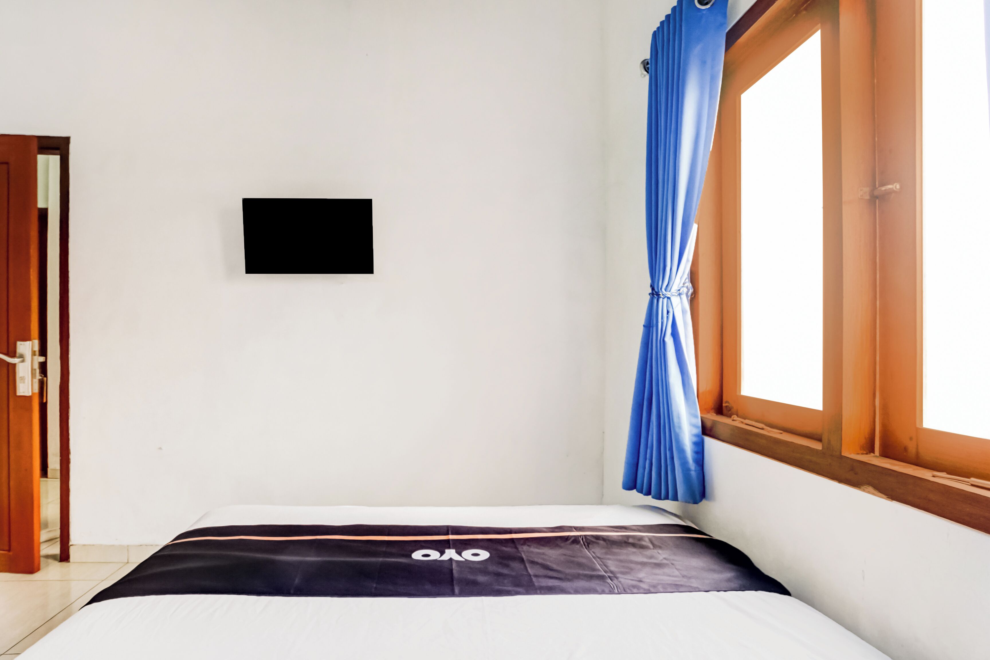 Een kamer met een bed, een tv aan de muur, een raam met blauwe gordijnen en een deur.