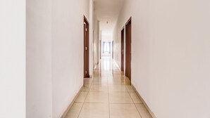 A long, narrow hallway with white walls and wooden doors, leading to a bright room at the end. - OYO 94780 Blessing Homestay (Surabaya)